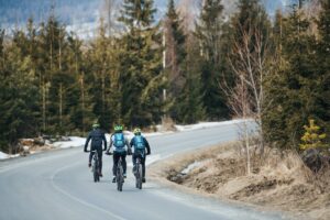 Rear view of mountain bikers riding on road in mountains outdoors in winter.